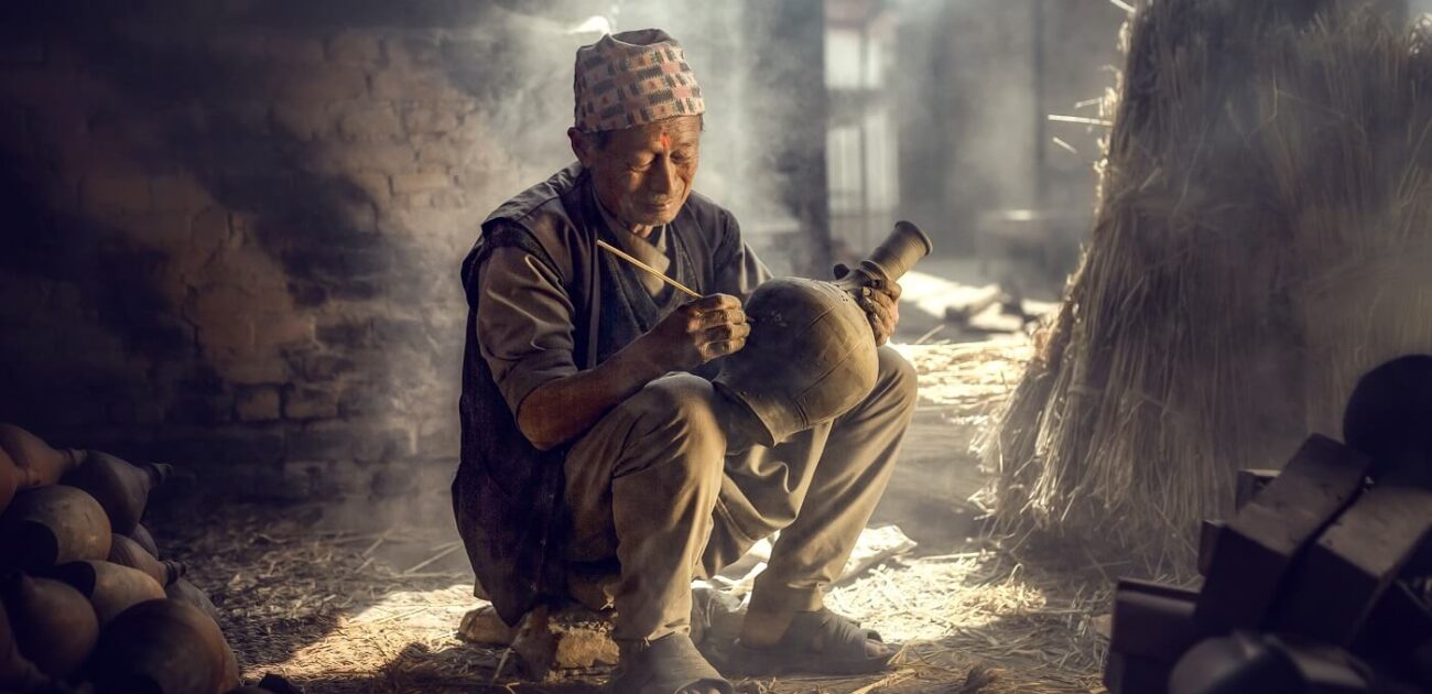 The old man is painting in a clay pot in Durbar square near old hindu temples.